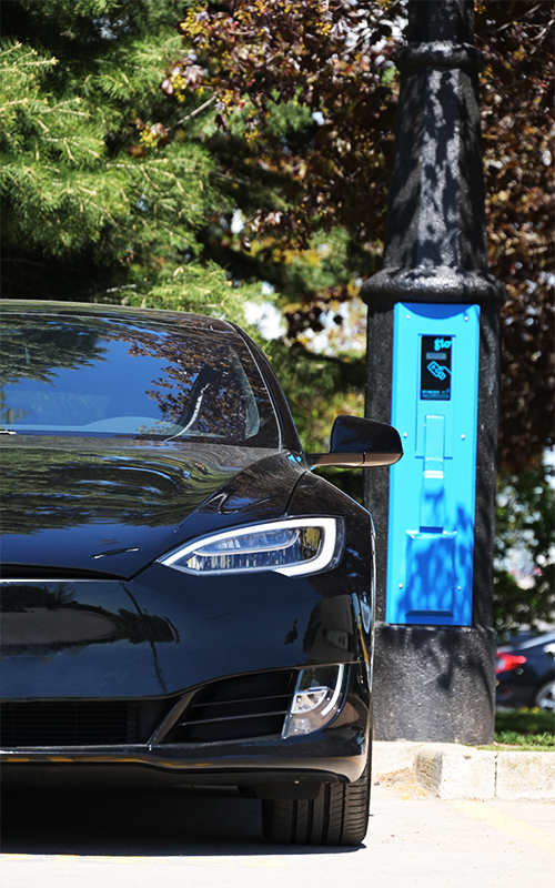 The VoltLock Concealed EV Charger Pole installed in a parking lot; pictured with an electric vehicle